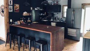 A modern kitchen with a central island, bar stools, and black cabinetry. - Cozy Cabin In The Woods  (Sprucedale)