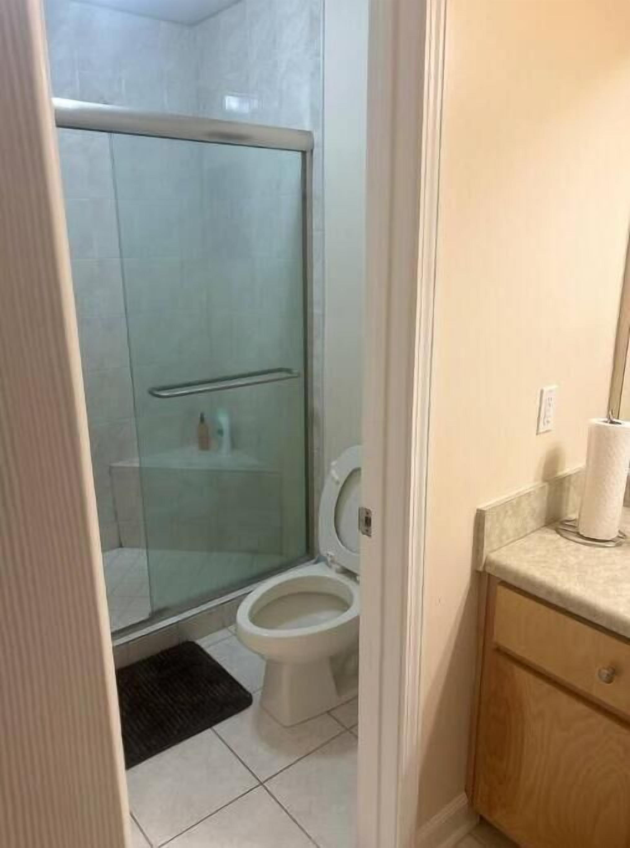 A bathroom with a glass shower enclosure, a toilet, and a wooden vanity with a towel dispenser.