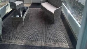 Een overdekt terras met rieten meubilair, een plafondventilator en uitzicht op een bebost gebied.