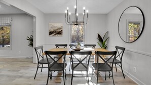 A dining area with a wooden table and black chairs, a chandelier, and a large mirror on the wall. - Large/Modern Home, Walk to Paris Mtn. State Park (Greenville)