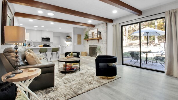 A spacious living area with a fireplace, a dining area with outdoor seating, and a kitchen with white cabinets. - Large/Modern Home, Walk to Paris Mtn. State Park (Greenville)