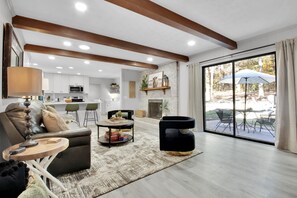 Un amplio espacio habitable con chimenea, un comedor con asientos exteriores y una cocina con gabinetes blancos.