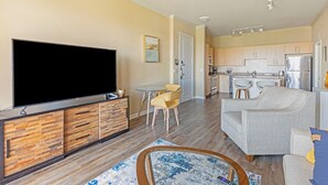 Una sala de estar moderna con un televisor de pantalla plana, un sofá y un comedor con sillas y una mesita.