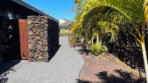 Un sendero de grava conduce a una entrada de pared de piedra con una puerta de madera.