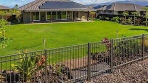Una propiedad residencial con un césped bien cuidado, una cerca de metal y una vista despejada del paisaje circundante.