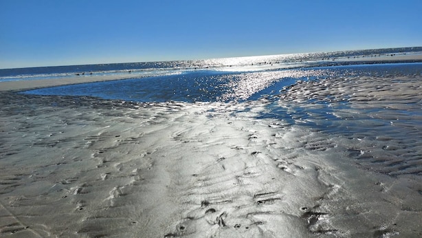 Ein Strand mit deutlichen Fußspuren und blauem Himmel.