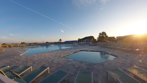 Ein Schwimmbeckenbereich mit mehreren Pools und Liegestühlen, umgeben von einer gepflasterten Terrasse.