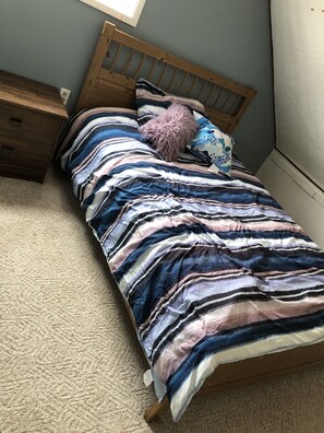 A single bed with a striped bedspread, a wooden headboard, a wooden nightstand, and a small drawer unit. - Cozy 2 Bedroom Apartment
Hardisty AB
Fully Equipped & =Furnished (Hardisty)