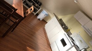 Una cocina con suelo de madera, armarios blancos y una zona de comedor con mesa y sillas de madera.