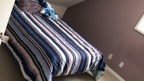 Un dormitorio con una cama bajo un techo inclinado, una pared morada y suelo alfombrado.