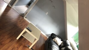 Una sala de estar con un sofá de cuero negro, una mesa de centro de madera y una mesita auxiliar blanca. Una puerta da a otra habitación.