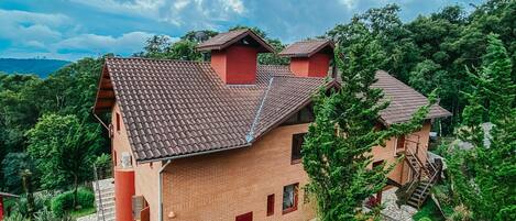 A brick house with a tiled roof, surrounded by lush greenery and large rocks.