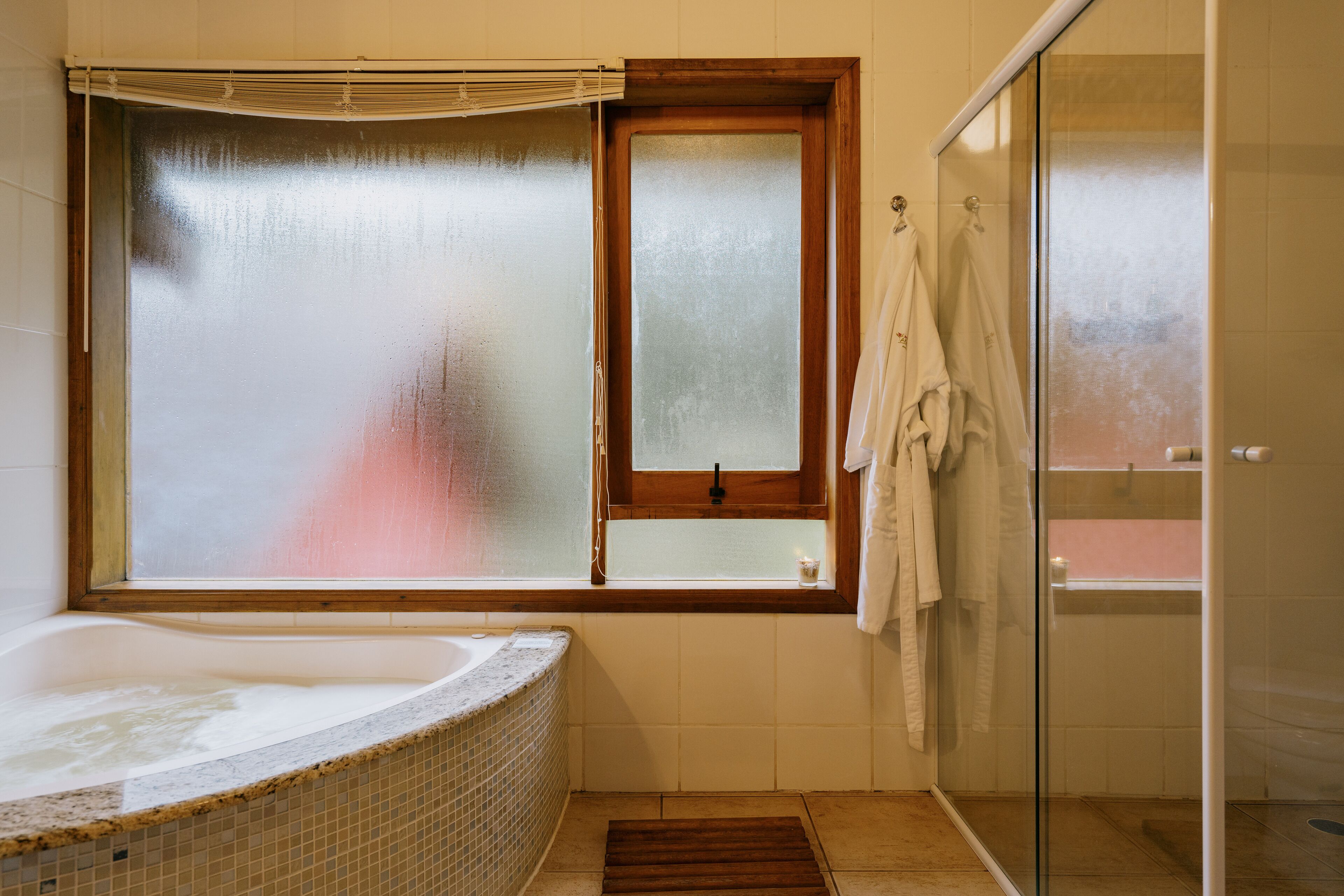 Un baño con bañera, una ventana con vidrio esmerilado, ducha y un perchero para toallas.