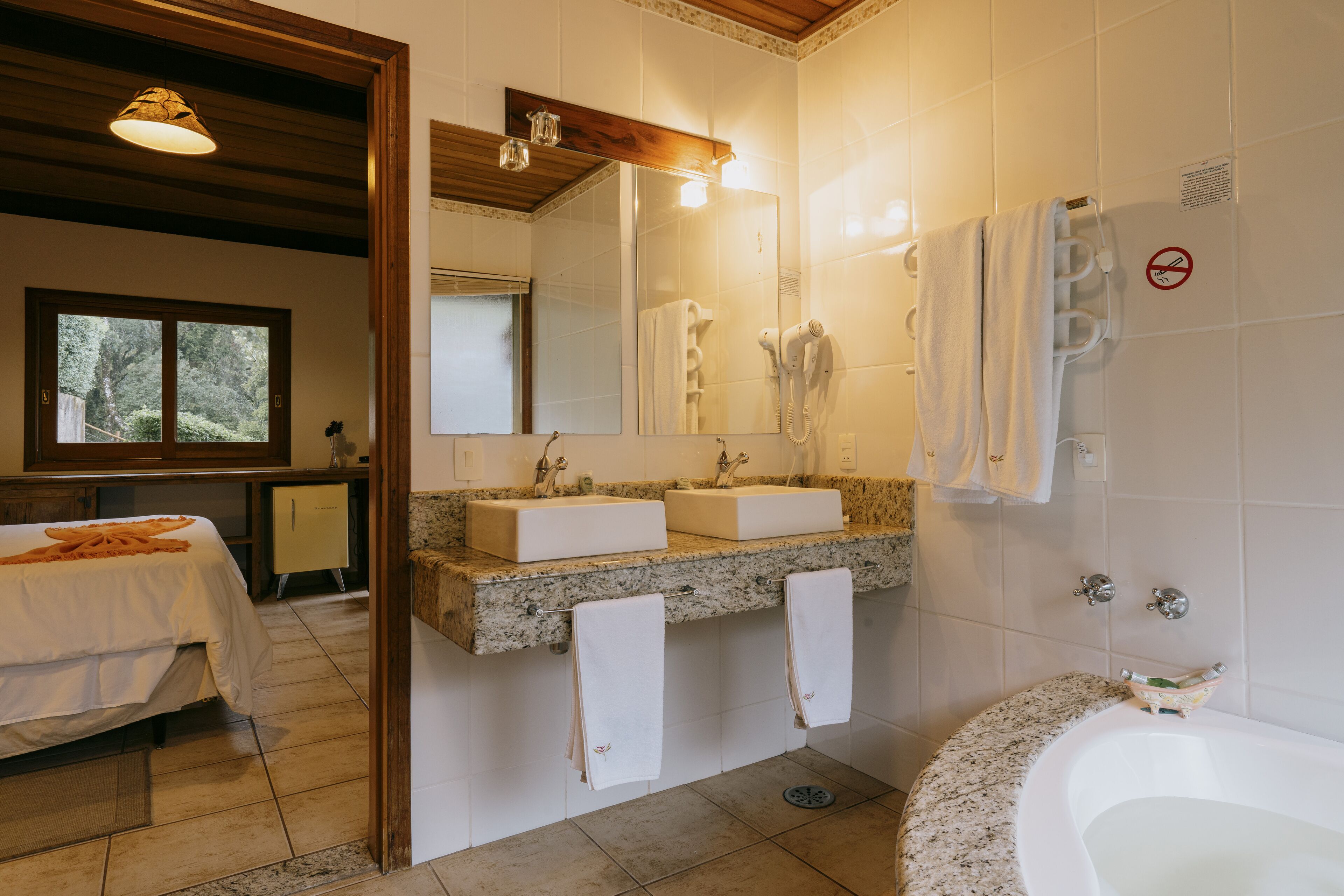Un baño con dos lavamanos, un espejo grande, una bañera y una ventana con vistas a árboles.