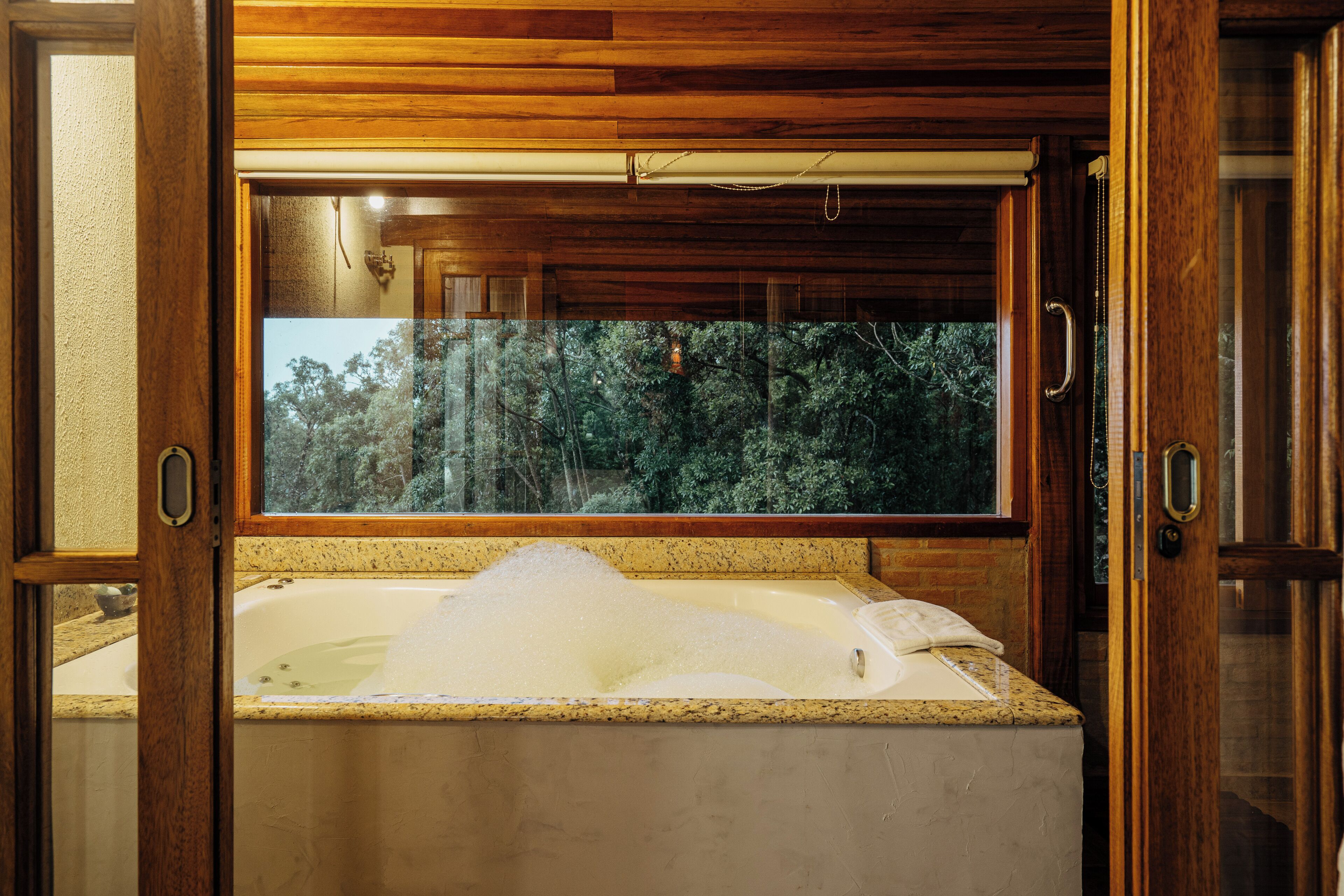 Un baño con bañera, techo de madera y ventana con vista a árboles.
