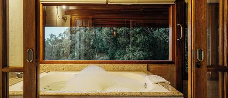 Un baño con bañera, techo de madera y ventana con vista a árboles.