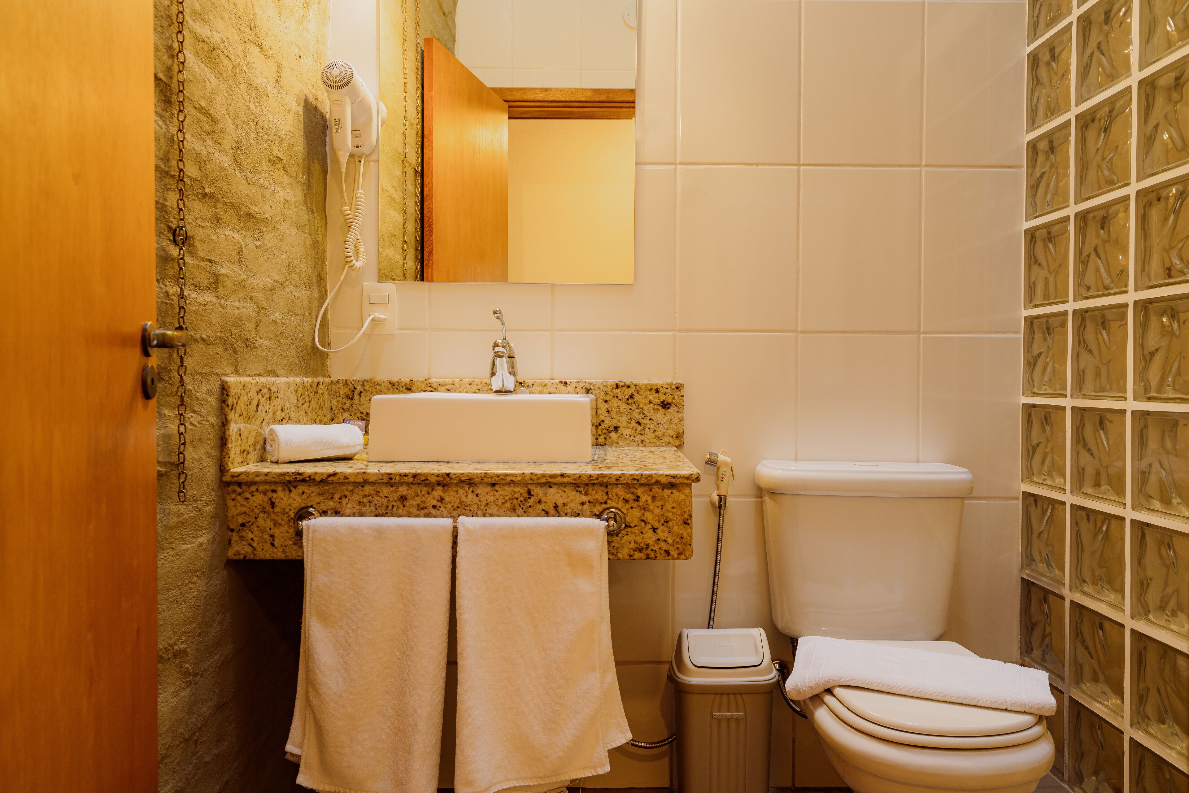A bathroom with a granite countertop, a white sink, a toilet, and a mirror above the sink. There are two towels hanging on the wall.