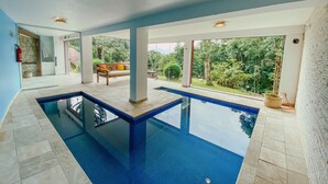 Una piscina interior con agua azul cristalina, rodeada de amplios ventanales que dan a un jardín exuberante.