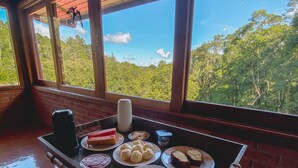 Una mesa de comedor con platos de comida y vistas al bosque a través de grandes ventanales.