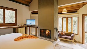 Un dormitorio con cama, televisión, chimenea y ventana con vistas a la vegetación.