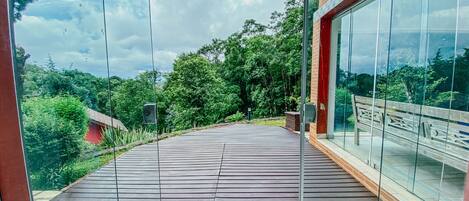 A modern outdoor deck with a glass balustrade overlooking a lush garden and trees.