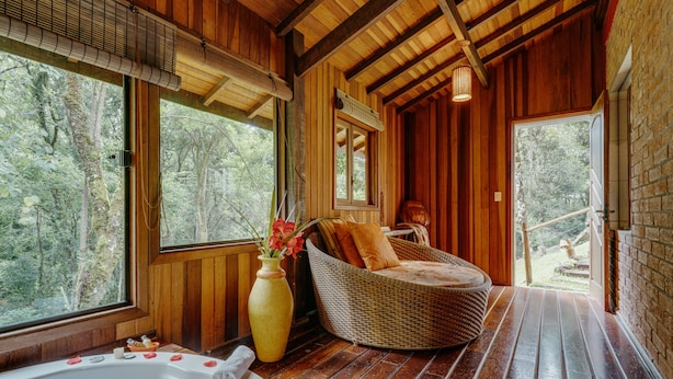 Un interior de madera con bañera de hidromasaje, muebles de mimbre y ventanas amplias con vistas a un bosque.