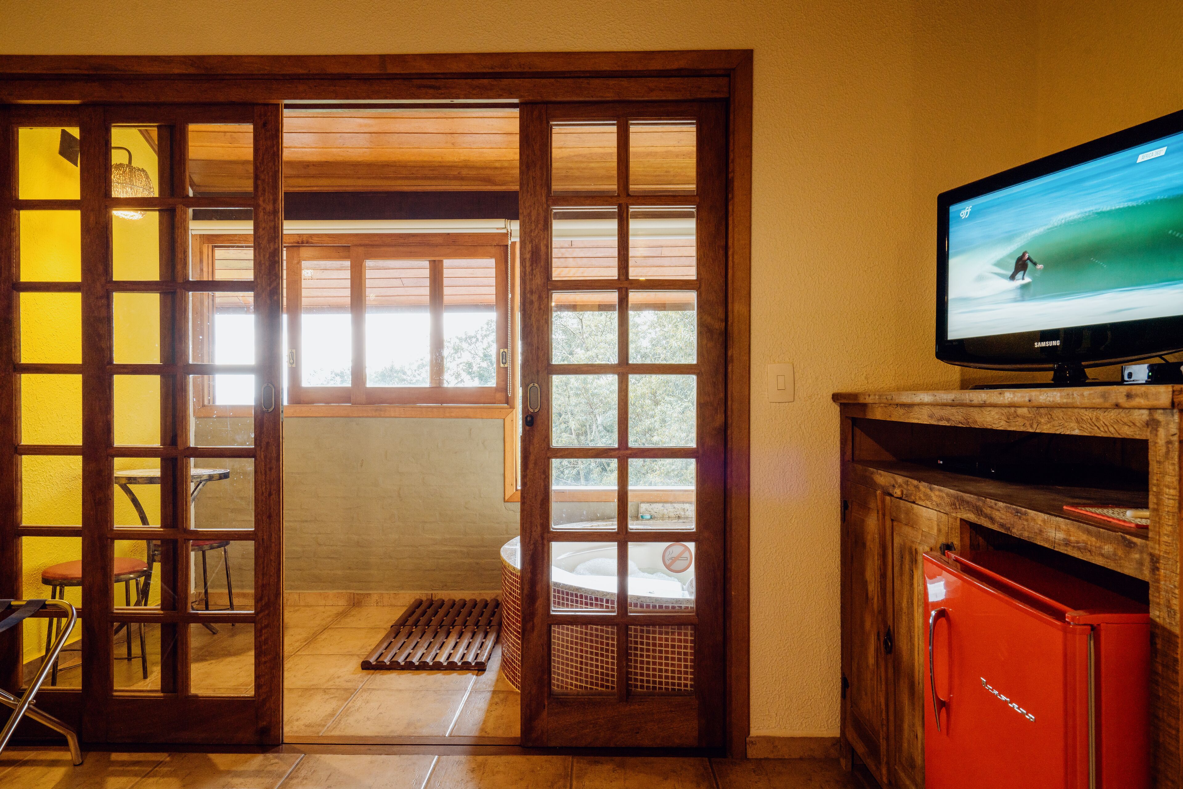 A room with a wooden sliding door leading to a balcony, a television on a wooden stand, and a red cabinet.