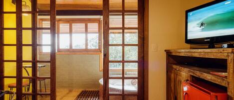 A room with a wooden sliding door leading to a balcony, a television on a wooden stand, and a red cabinet.