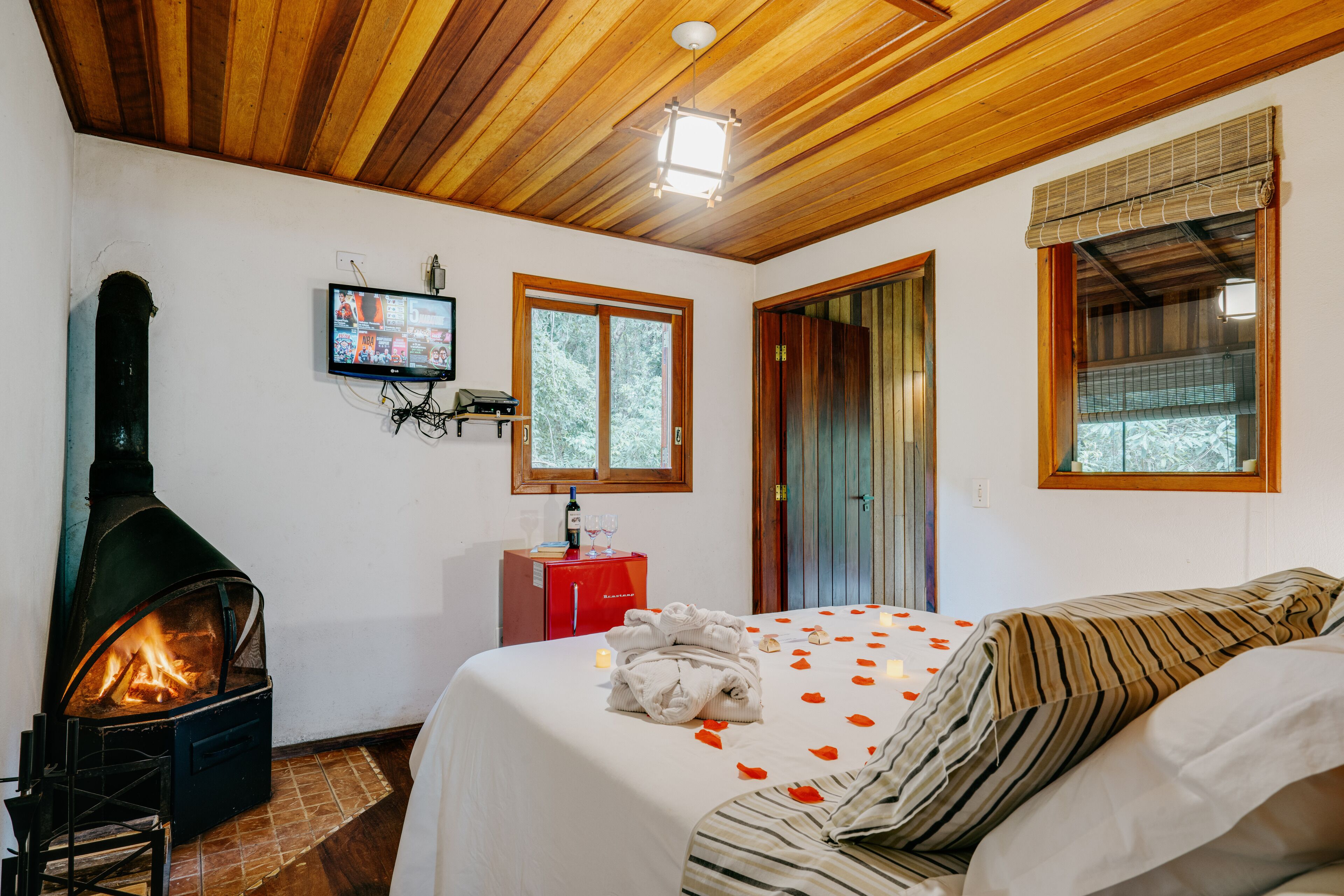 Ein gemütliches Zimmer mit Kaminofen, einem Bett mit Rosenblättern und einem Fernseher an der Wand.