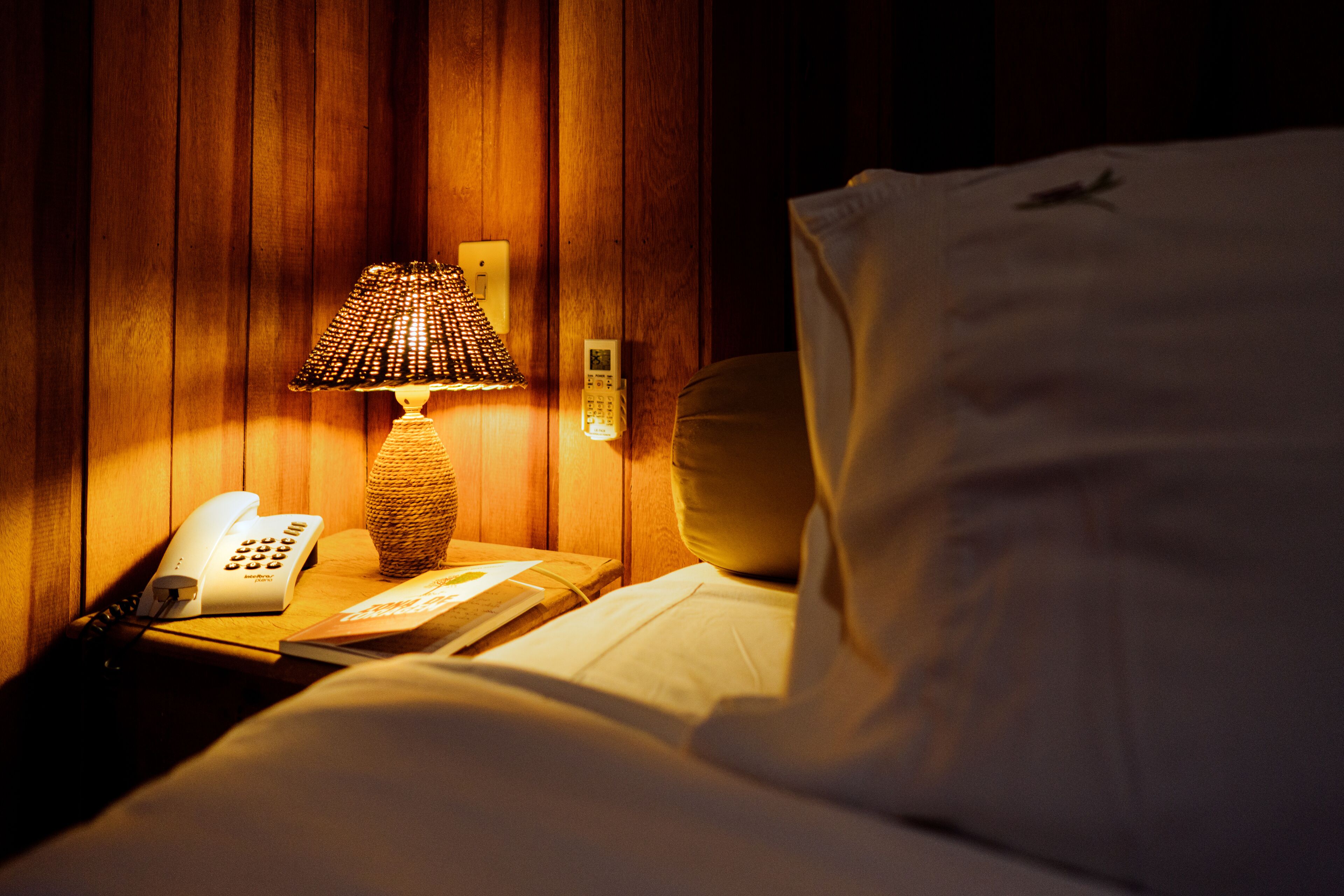 Een hotelkamer met een houten wand, een bedlampje, een telefoon en een bed met een kussen.