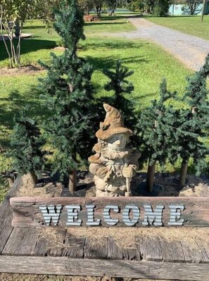 Set against a lush lawn, the property's entrance features a welcoming sign and two evergreen trees.