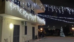 Un bâtiment doté d’un balcon décoré de guirlandes lumineuses, d’un petit sapin de Noël et d’une allée gravillonnée.