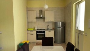 Un coin repas avec une table et des chaises, une cuisine en arrière-plan et une fenêtre avec un rideau.