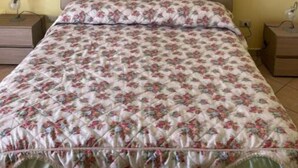 Une chambre à coucher avec une couvre-lit à motifs floraux, deux oreillers et une table de chevet avec une lampe.