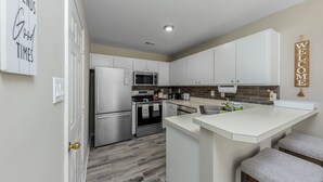 Une cuisine moderne avec des meubles blancs, un four encastré, un four à micro-ondes et un grand îlot central doté de tabourets.