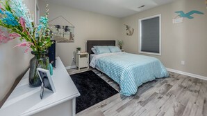 Une chambre à coucher comprenant un lit, une table de chevet, une commode et une fenêtre avec des stores.