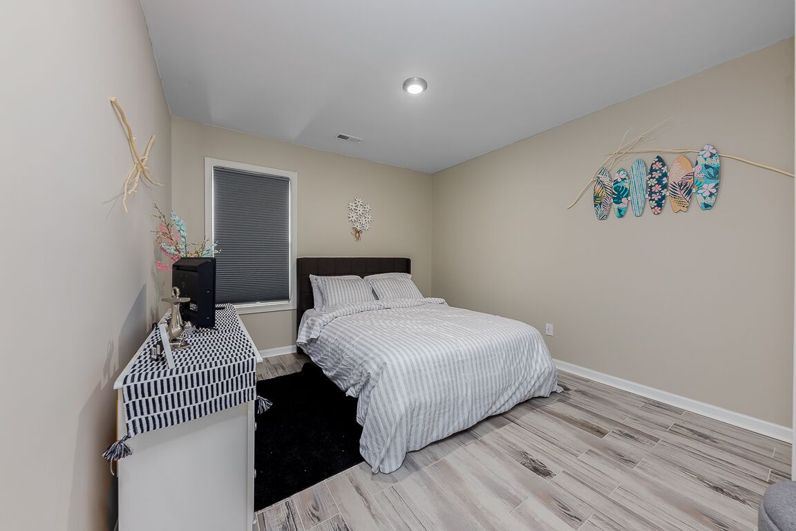 A bedroom with a bed, a dresser, a window with blinds, a ceiling light, and wall decorations.