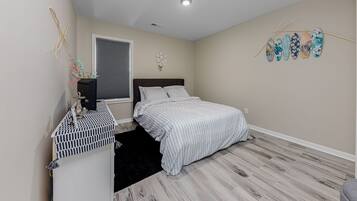 A bedroom with a bed, a dresser, a window with blinds, a ceiling light, and wall decorations.