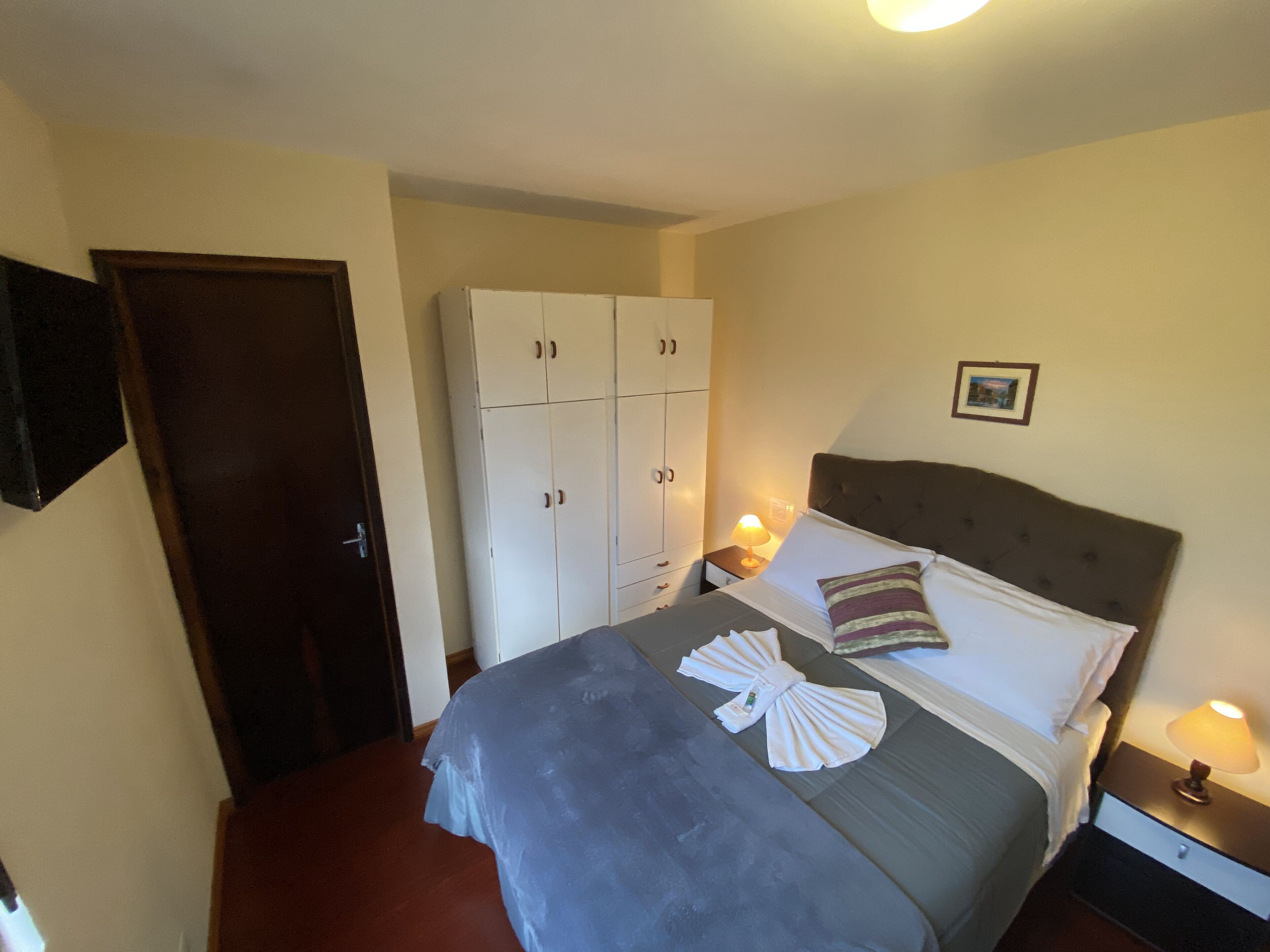 A hotel room with a bed, a wardrobe, a nightstand, and a wall-mounted picture.