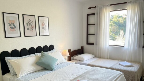 A hotel room with two beds, a window with curtains, and three framed botanical prints on the wall.