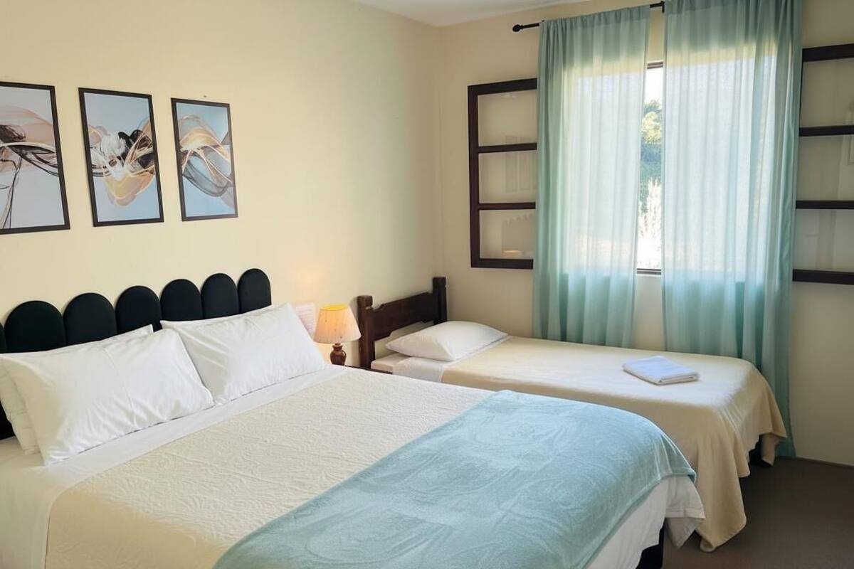 Una habitación de hotel con dos camas, un ventanal con cortinas y tres cuadros en la pared.