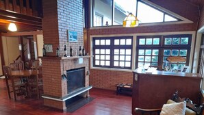 A spacious living area with a brick fireplace, wooden furniture, and large windows offering natural light.