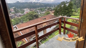 A balcony with a wooden railing overlooking a town with traditional houses and a mountainous backdrop.