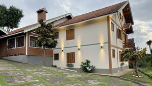 A two-story house with a tiled roof, a brick chimney, and a paved front yard with grass and stone tiles.