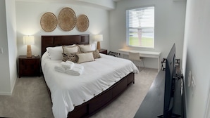 A bedroom with a large bed, two bedside tables with lamps, a desk, and a TV.