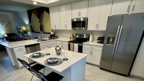 A modern kitchen with white cabinetry, stainless steel appliances, and a central island with seating.