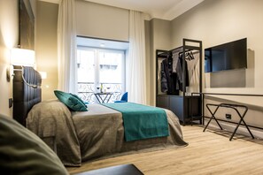 Quarto de hotel com cama, televisão, guarda-roupa e janela com cortinas.