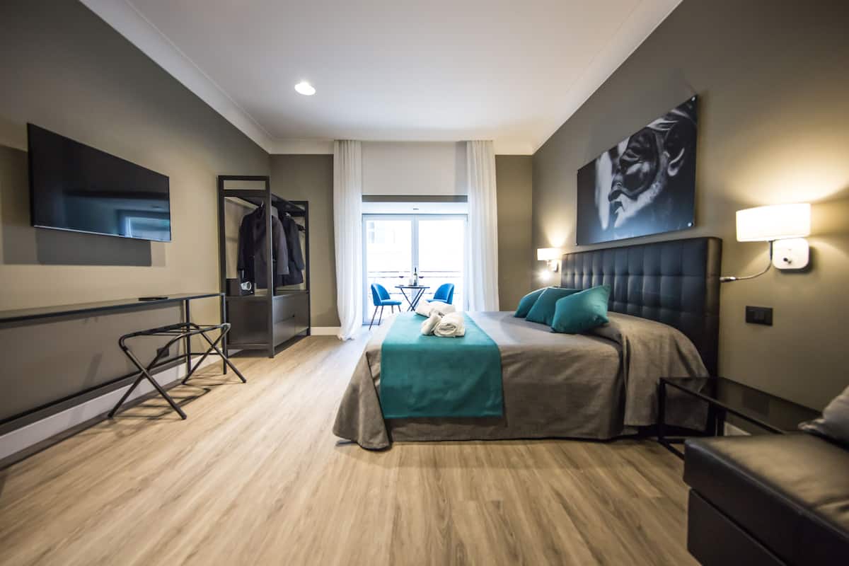 A modern hotel room with a large bed, a flat-screen TV, a dining area, and a view of the outdoors.