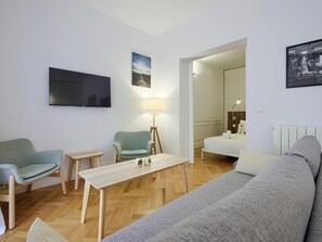 A modern living room with a sofa, two armchairs, a small table, and a TV mounted on the wall.