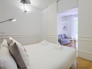 Una cama bien hecha con sábanas blancas y una lámpara en la mesita de noche.